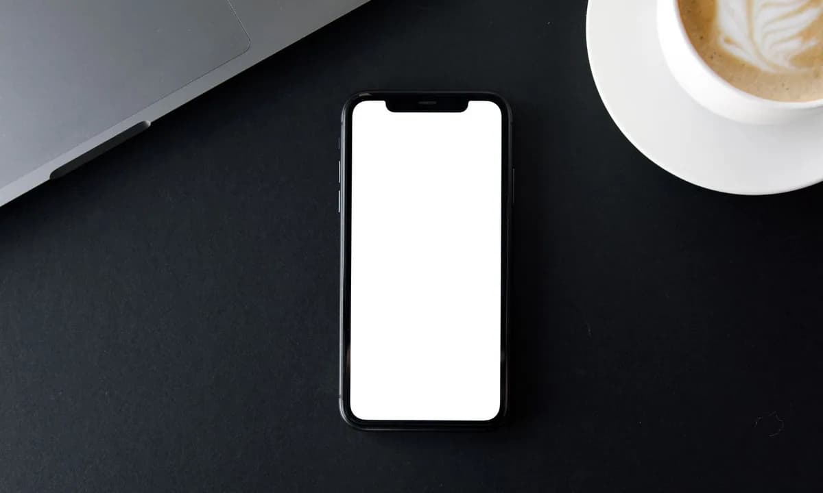 Koyu renk çalışma masasında beyaz ekranlı telefon ve kahve fincanı
