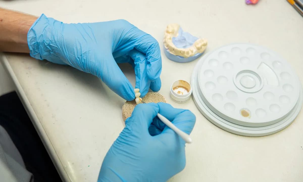 Dental modele fırçayla ayrıntı uygulayan eldivenli eller